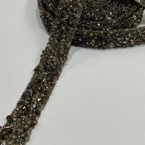 May include: A roll of silver-toned beaded trim with a sparkly finish. The trim is made of small, faceted beads that are sewn together in a continuous line.