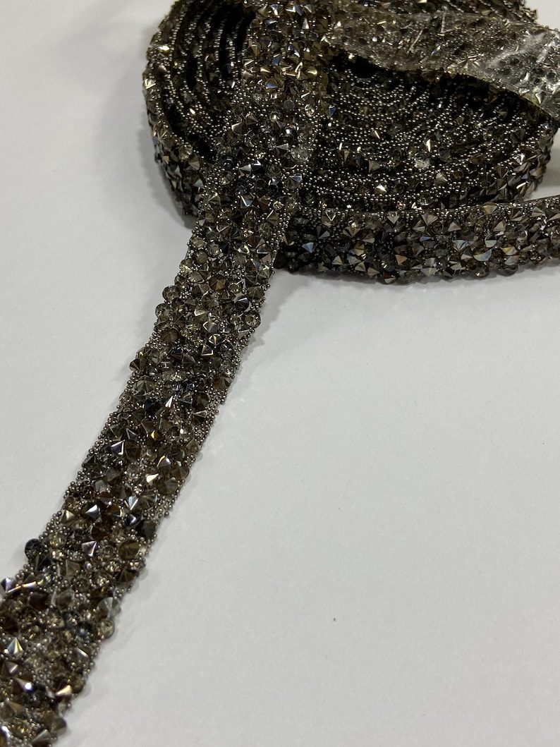 May include: A roll of silver-toned beaded trim with a sparkly finish. The trim is made of small, faceted beads that are sewn together in a continuous line.