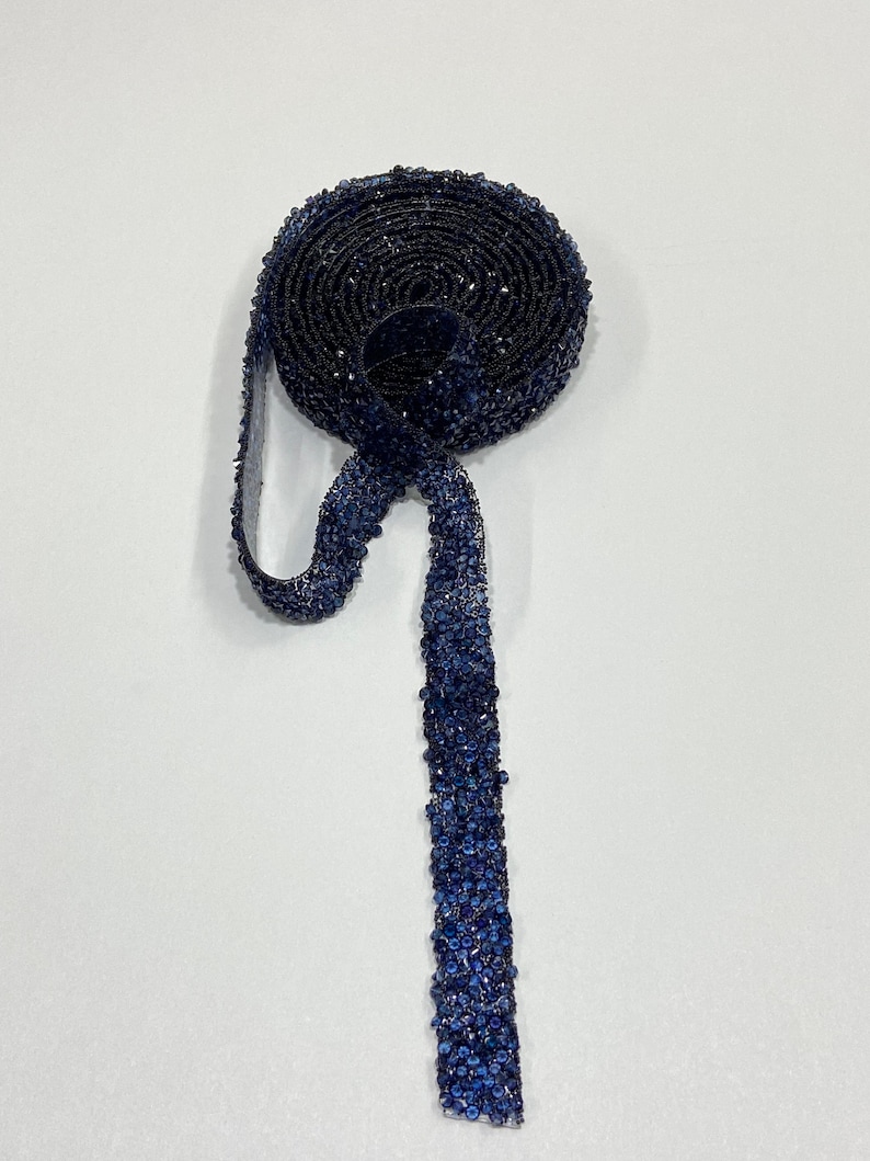 May include: A roll of dark blue beaded trim with a long strand of the trim hanging down.