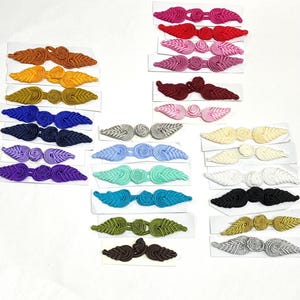 Puede incluir: Surtido de 20 botones o cierres de tela en forma de hoja de diferentes colores. Los cierres están hechos de tela trenzada y tienen un centro anudado. Los colores incluyen rojo, rosa, morado, azul, verde, amarillo, naranja, marrón, negro, blanco y plateado.