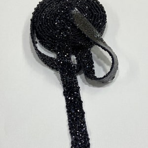May include: A roll of black beaded trim with a shiny finish. The trim is made of small, faceted beads that are sewn together in a continuous line.