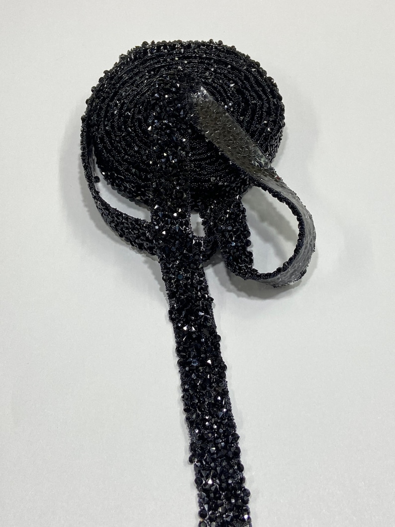 May include: A roll of black beaded trim with a shiny finish. The trim is made of small, faceted beads that are sewn together in a continuous line.