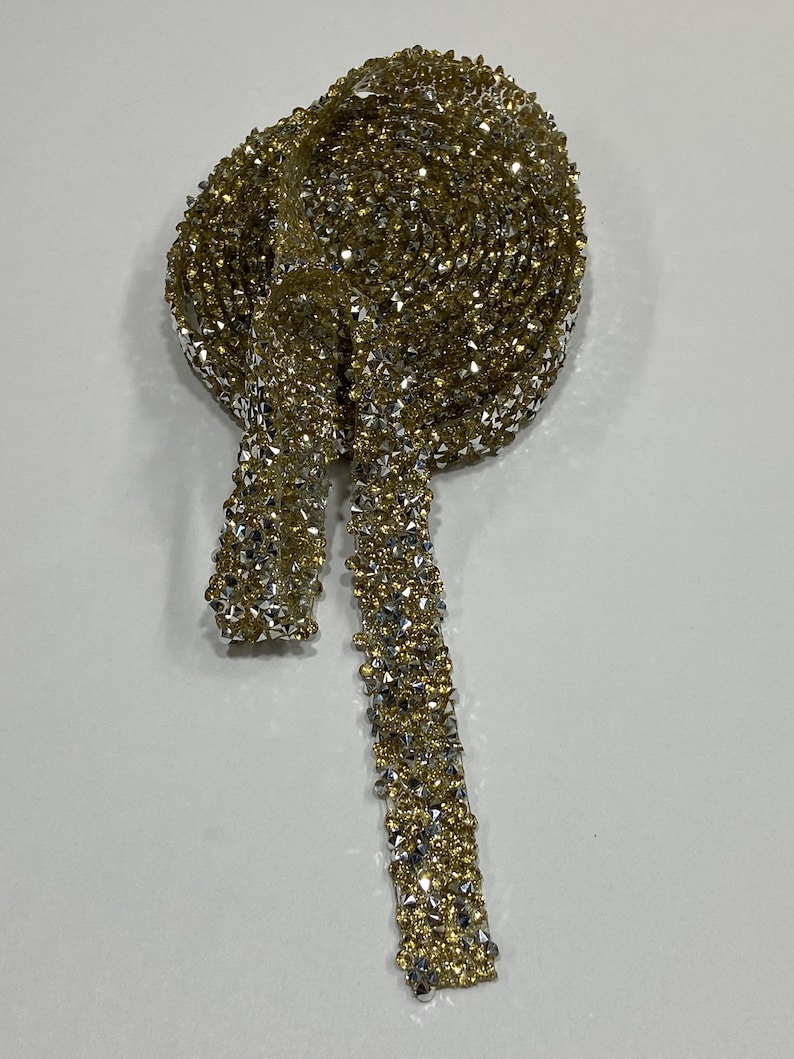 May include: A gold and silver rhinestone trim with a sparkly finish. The trim is rolled up and a long piece is hanging down.