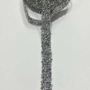 May include: Silver rhinestone trim with a sparkly finish. The trim is rolled up and a section is unrolled to show the detail.