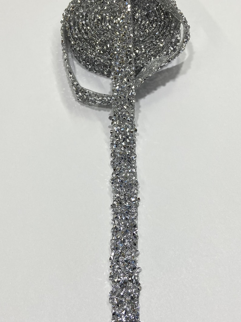 May include: Silver rhinestone trim with a sparkly finish. The trim is rolled up and a section is unrolled to show the detail.