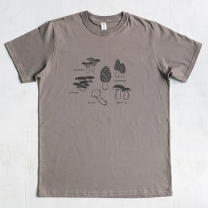 May include: A heather grey t-shirt with a graphic of different types of mushrooms. The mushrooms are labeled in Japanese with the names: "アンズタケ", "アミガサタケ", "ミョウガ", "マツタケ", and "ポルチーニ".