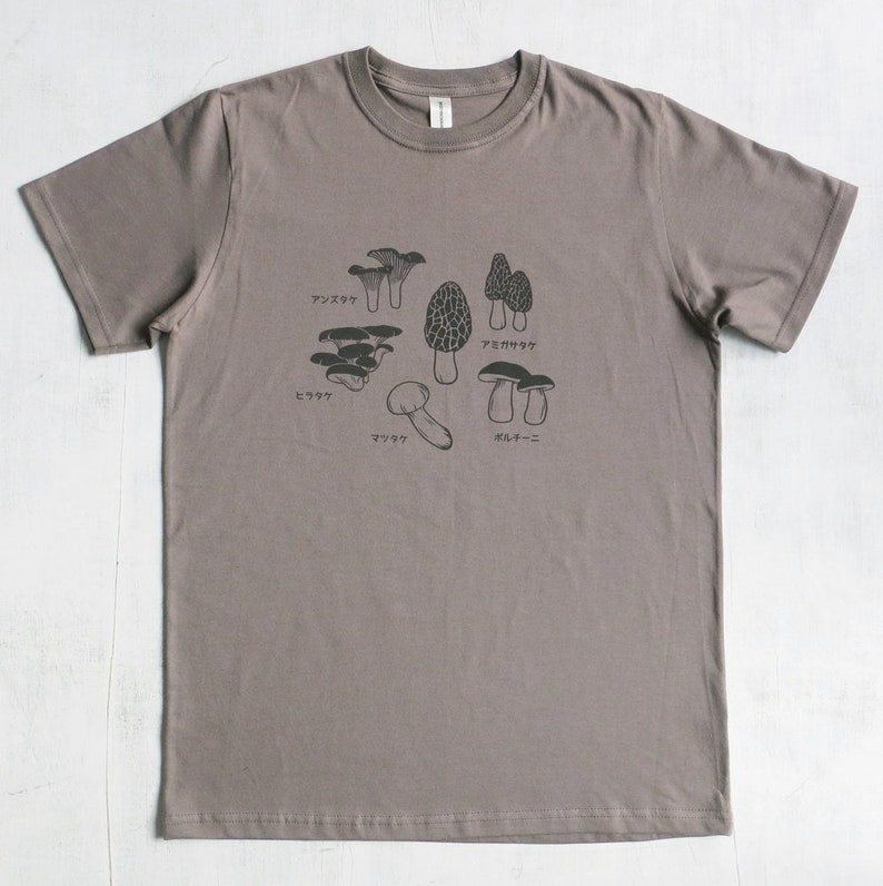 May include: A heather grey t-shirt with a graphic of different types of mushrooms. The mushrooms are labeled in Japanese with the names: "アンズタケ", "アミガサタケ", "ミョウガ", "マツタケ", and "ポルチーニ".