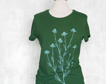 Könnte beinhalten: Ein dunkelgrünes Kurzarm-T-Shirt mit einem hellblauen Grafikdruck einer Ansammlung von Kamillenblüten mit dünnen Stielen und zarten Blättern, die mittig auf der Vorderseite des Kleidungsstücks platziert sind und auf einem Torso-Mannequin präsentiert werden.