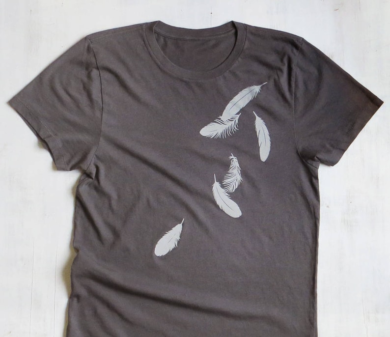 May include: A dark gray t-shirt with a white feather design. The feathers are scattered across the shirt in a random pattern.