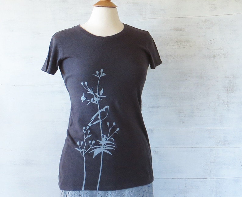 May include: A dark grey t-shirt with a light blue floral design on the left side.