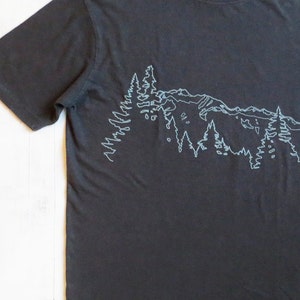 May include: A dark grey t-shirt with a white outline of a mountain range and trees.