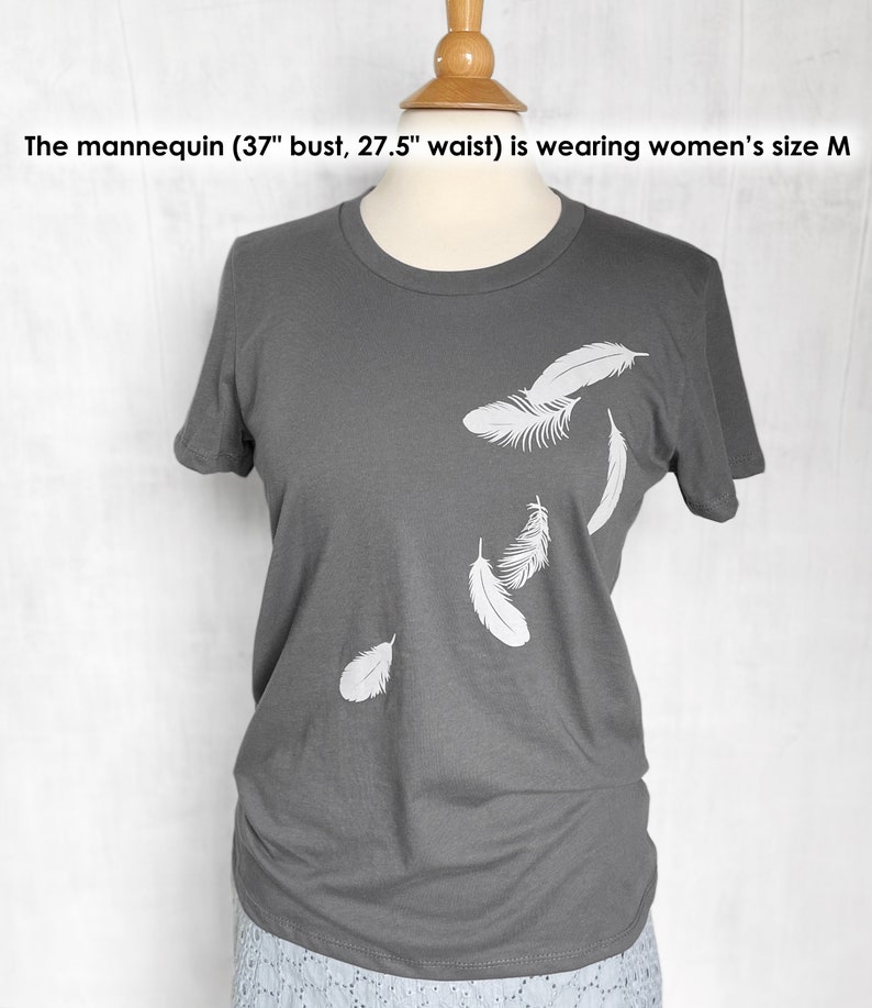 May include: A gray t-shirt with a white feather design. The mannequin is wearing a size M.