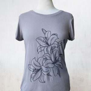 May include: A gray t-shirt with a black floral design featuring lilies. The lilies are stylized and have a simple, elegant look.