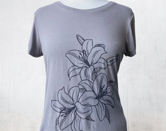 Könnte beinhalten: Ein graues T-Shirt mit einem schwarzen Blumendesign mit Lilien. Die Lilien sind stilisiert und haben einen schlichten, eleganten Look.