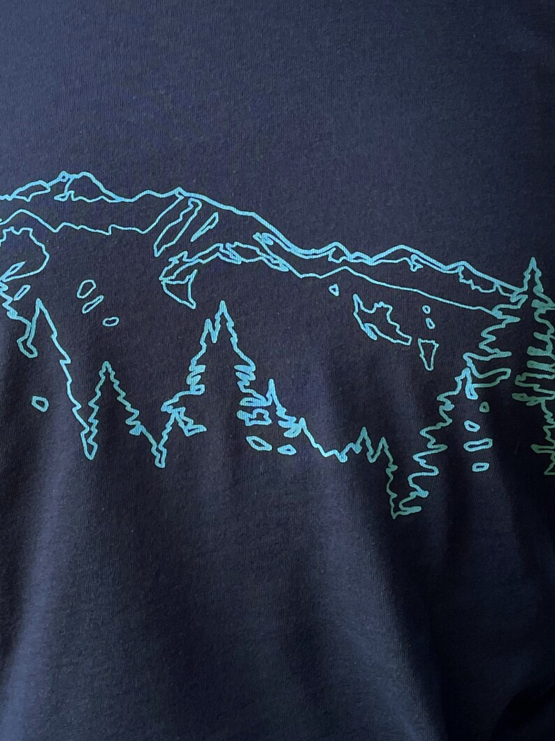 May include: A navy blue t-shirt with a light blue outline of a mountain range and trees.