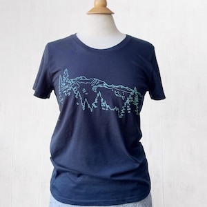 May include: A dark blue t-shirt with a green line drawing of a mountain range and trees.
