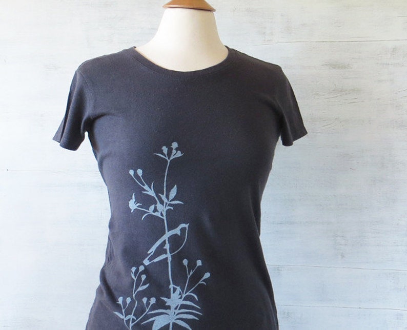 May include: A dark grey t-shirt with a light blue floral design on the left side of the shirt.