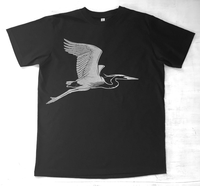 May include: A black t-shirt with a white silhouette of a heron in flight.