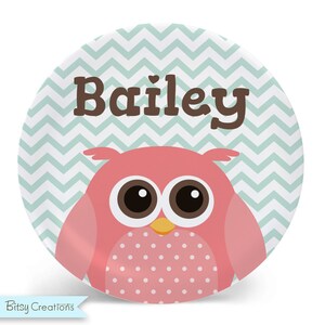 May include: A personalized pink owl plate with a teal chevron pattern and the name "Bailey" printed in brown letters.