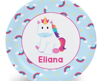 May include: A blue and white personalized plate with a rainbow and cloud pattern. The center of the plate features a cartoon unicorn with a rainbow mane and tail. The name "Eliana" is printed in pink below the unicorn.
