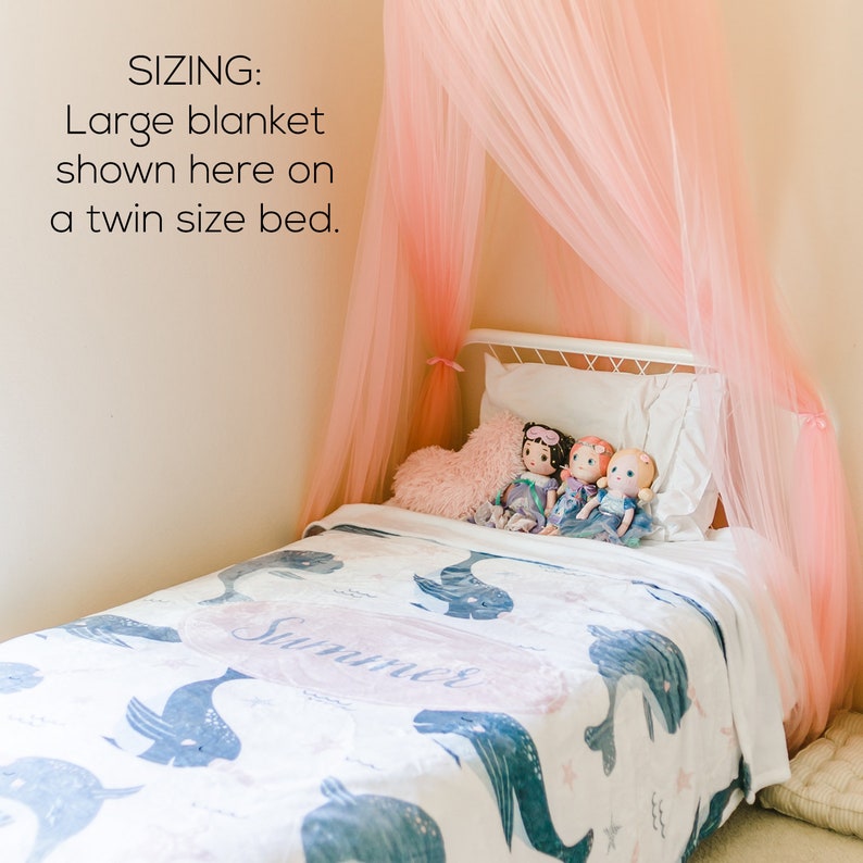 Pu&ograve; includere: Un letto bianco a una piazza con una baldacchino rosa e una coperta di balena blu e bianca. La coperta ha il nome "Summer" scritto su di essa. Tre bambole sono sedute sul letto.