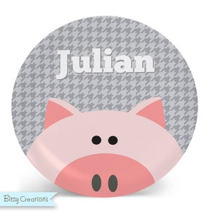 May include: A round, gray and white patterned plate with a pink pig face and the name "Julian" in white letters.