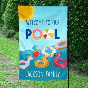 May include: A blue and yellow welcome to our pool sign with a sun, a beach ball, and inflatable pool toys. The sign says "Welcome to our Pool Jackson Family".
