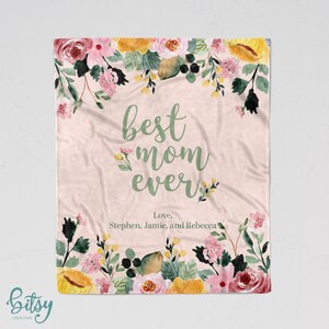 Pu&ograve; includere: Una coperta in pile rosa con motivo floreale e il testo "best mom ever" in corsivo verde. Il testo "Love, Stephen, Jamie, and Rebecca" &egrave; scritto sotto il testo principale.