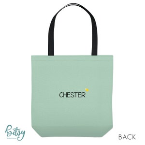 May include: A light green tote bag with black handles and the word "CHESTER" embroidered in black with a small yellow star above the word.