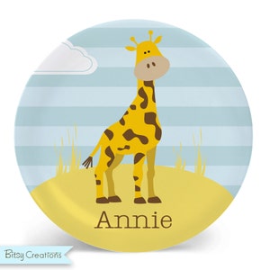May include: A yellow and brown giraffe stands on a yellow background with blue and white stripes. The name "Annie" is written below the giraffe.