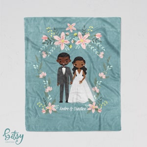 May include: A teal blue fleece blanket with a floral wreath design. The wreath is made of pink and yellow flowers. Inside the wreath is a cartoon illustration of a bride and groom. The bride is wearing a white dress and the groom is wearing a black suit. The text "Andre & Candice" is written below the couple.