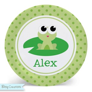 May include: Green and white personalized plate with a green frog on a lily pad. The plate has a green polka dot pattern and the name "Alex" is printed in green.