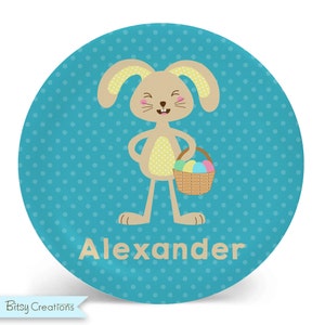 May include: A blue and yellow personalized Easter bunny plate with white polka dots. The bunny is holding a basket of colorful Easter eggs. The plate says "Alexander" in brown text.
