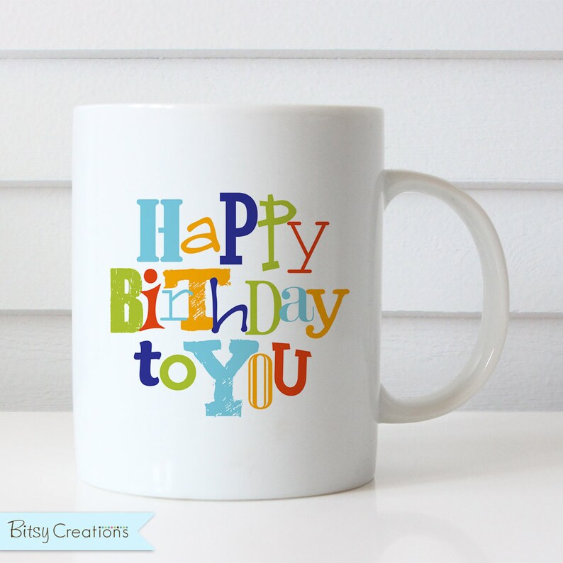 Puede incluir: Taza de caf&eacute; de cer&aacute;mica blanca con un dise&ntilde;o colorido de "Feliz cumplea&ntilde;os para ti". Las letras son de diferentes colores y fuentes, creando un aspecto divertido y festivo.