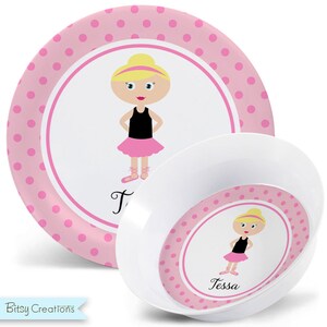 May include: Pink and white children's dinnerware set with a ballerina design. The set includes a plate and a bowl. The plate has pink polka dots and the bowl has a pink rim with pink polka dots. The ballerina is wearing a pink tutu and black shoes. The name "Tessa" is written on the bowl.