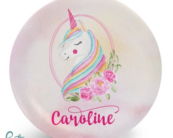 May include: A pink and white round plate with a watercolor design of a unicorn with a rainbow mane and flowers. The plate has the name "Caroline" written in pink cursive.
