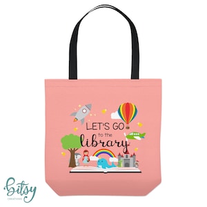 May include: Pink canvas tote bag with black handles. The bag features a colorful illustration of a book with a rocket, hot air balloon, airplane, and a rainbow. The text "Let's Go to the Library" is printed on the bag.