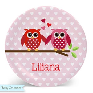 May include: Pink and red owl design on a pink background with white hearts. The owls are holding hands and there are hearts floating above them. The name "Lilliana" is written in red below the owls.