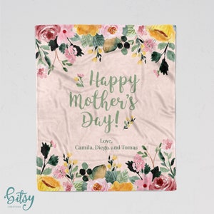 Pu&ograve; includere: Una coperta rosa con motivo floreale e il testo "Happy Mother's Day! Love, Camila, Diego, and Tomas" in lettere verdi.