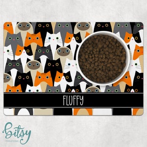 Pode incluir: Um tapete para tigelas de animais de estima&ccedil;&atilde;o com tema de gato preto e branco com uma tigela branca e comida para animais de estima&ccedil;&atilde;o marrom. O tapete tem uma borda preta com o nome "FLUFFY" impresso em branco.