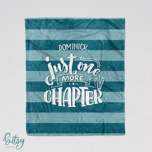 May include: Teal and light blue striped fleece blanket with the text "Just one more chapter" in white with a banner above the text that says "more" and the name "Dominick" at the top of the blanket.
