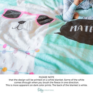 May include: A white fleece blanket with a llama wearing pink sunglasses and a black speech bubble with the word "MATH" printed on it. The blanket has a turquoise and white striped pattern.
