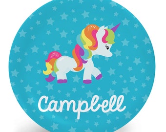 May include: A blue round plate with a white unicorn with a rainbow mane and tail. The plate has a blue background with white stars and the name "campbell" written in white.