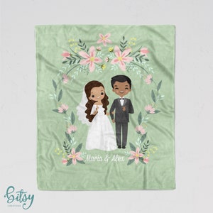 May include: A green fleece blanket with a floral wreath design. The wreath features pink flowers and green leaves. Inside the wreath is a cartoon illustration of a bride and groom. The bride is wearing a white dress and the groom is wearing a black suit. The text "Maria & Alex" is written below the couple.