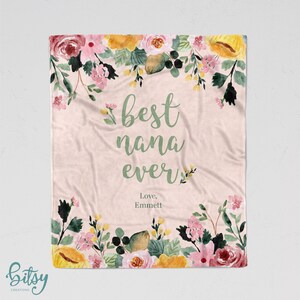 Pu&ograve; includere: Una coperta rosa con motivo floreale e il testo "best nana ever" in lettere verdi. Il testo "Love, Emmett" &egrave; scritto sotto il testo principale.