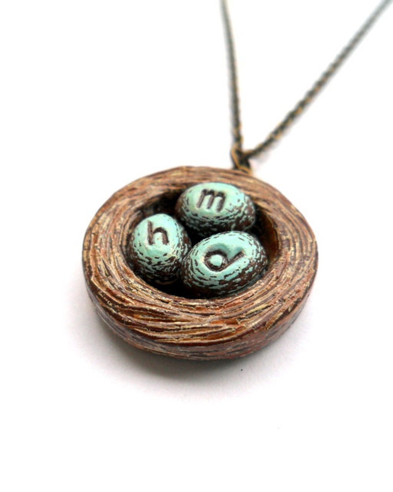 May include: A brown ceramic bird's nest necklace with three teal blue eggs that have the letters 'h', 'o', and 'm' on them.