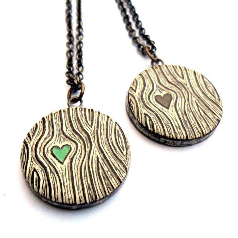 May include: Two round pendant necklaces with a wood grain design and a heart-shaped cutout. One heart is green, the other is brown. The pendants hang from a dark chain.