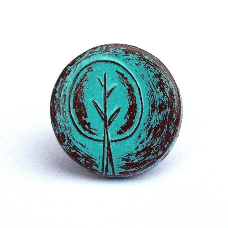 May include: A round turquoise and brown ceramic knob with a stylized tree design.
