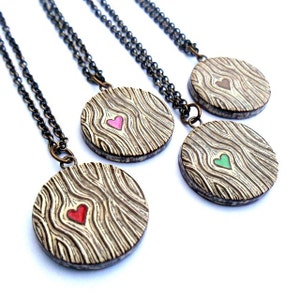 May include: Four round pendant necklaces with a wood grain design and a colored heart in the center. The hearts are red, pink, brown, and green. The necklaces have dark metal chains.