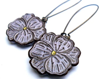May include: A pair of earrings featuring a purple flower design with a gold center. The earrings are made of metal and have a simple, elegant style.